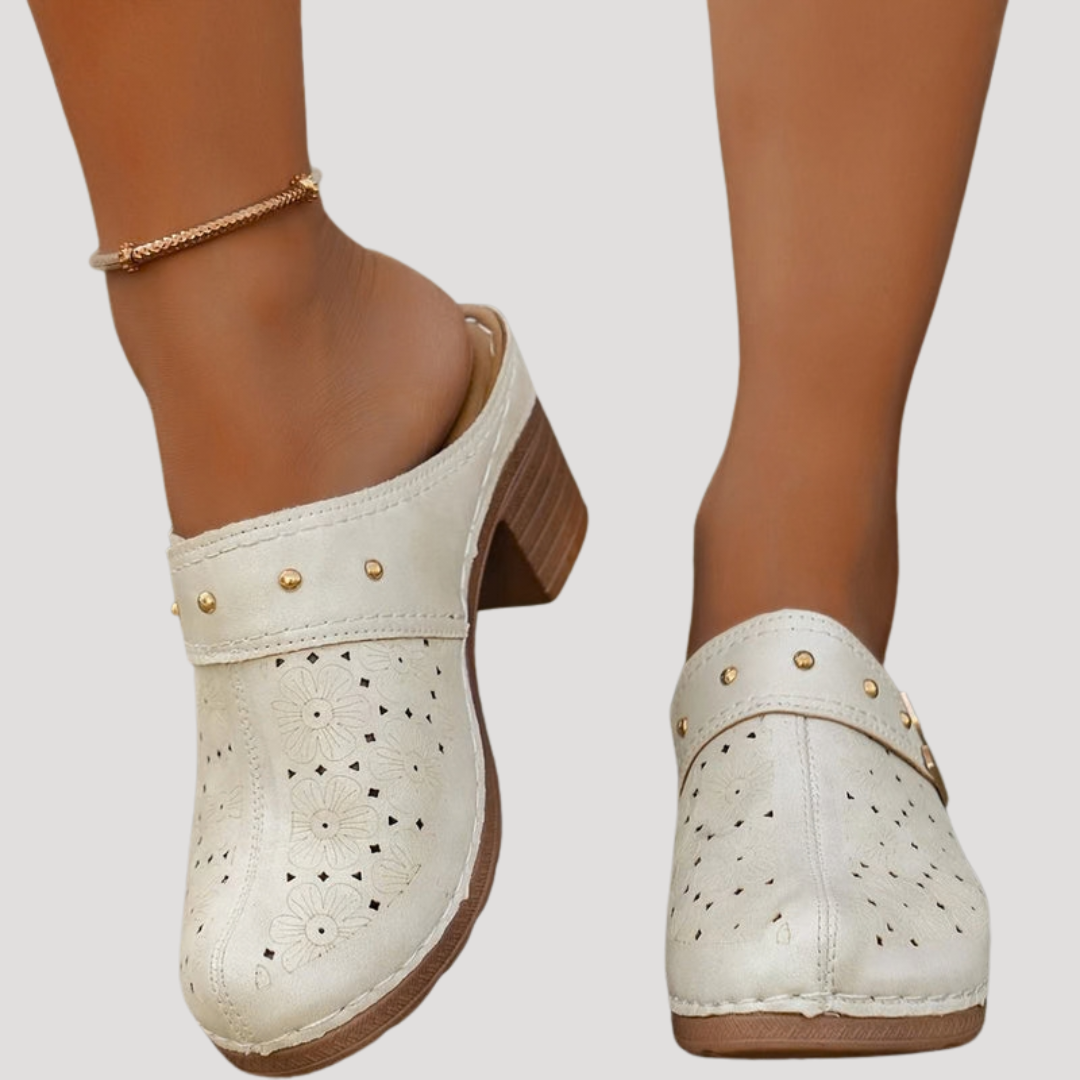Cream leather clog mules featuring perforated floral pattern and studded strap