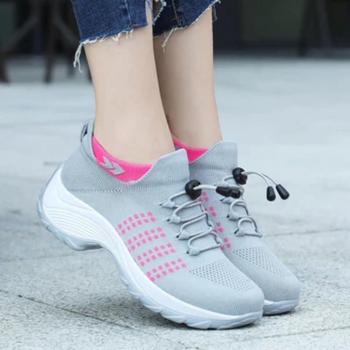 gray sneakers with pink accents worn on feet with toggle laces
