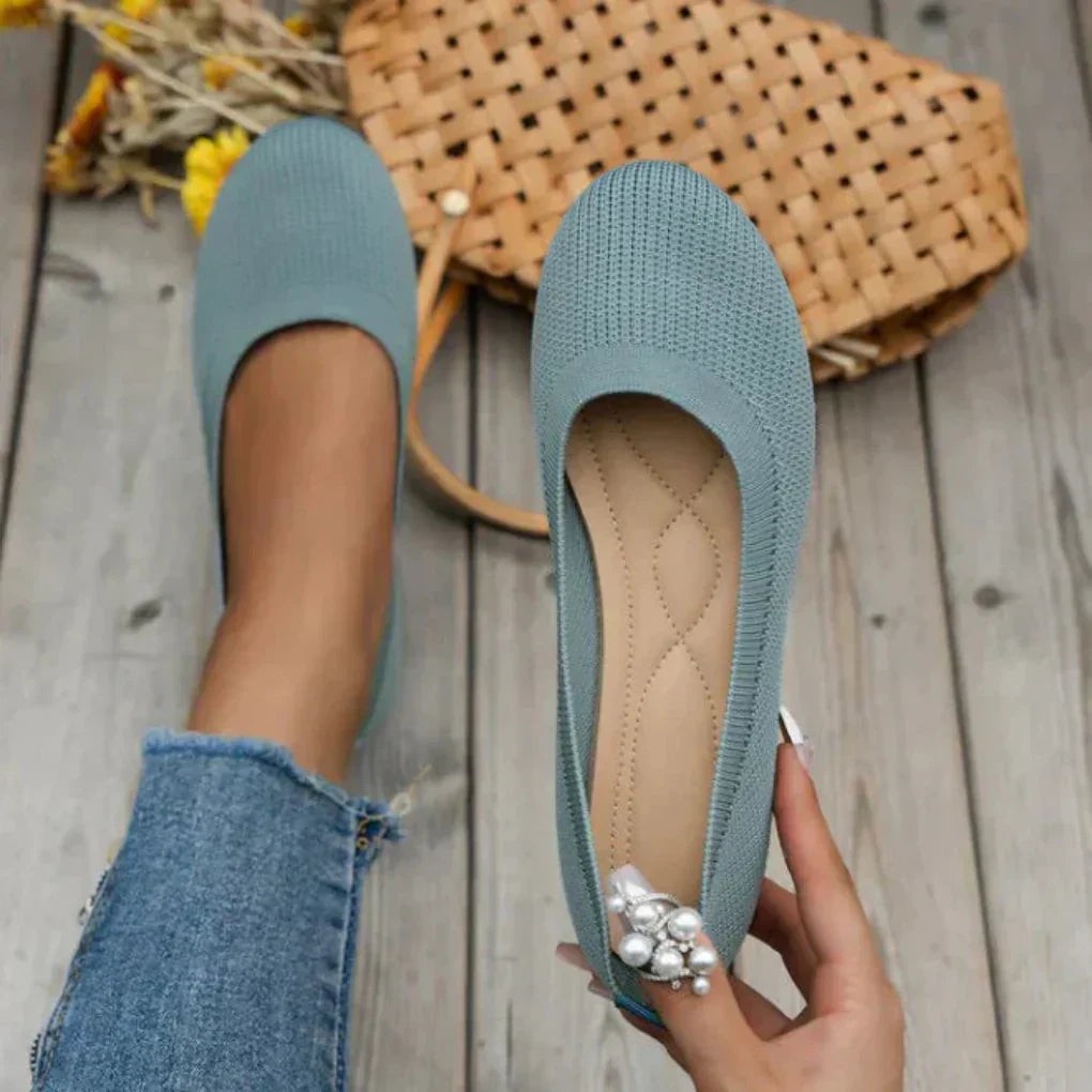 Sage green knit slip-on flats with quilted insole beside woven straw bag