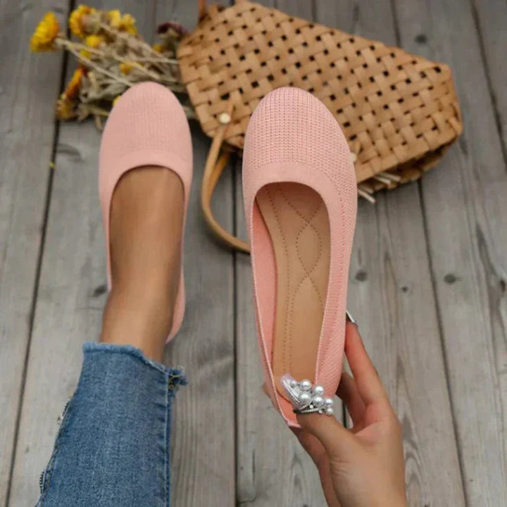 Blush pink knit ballet flats with quilted insole displayed on wood planks