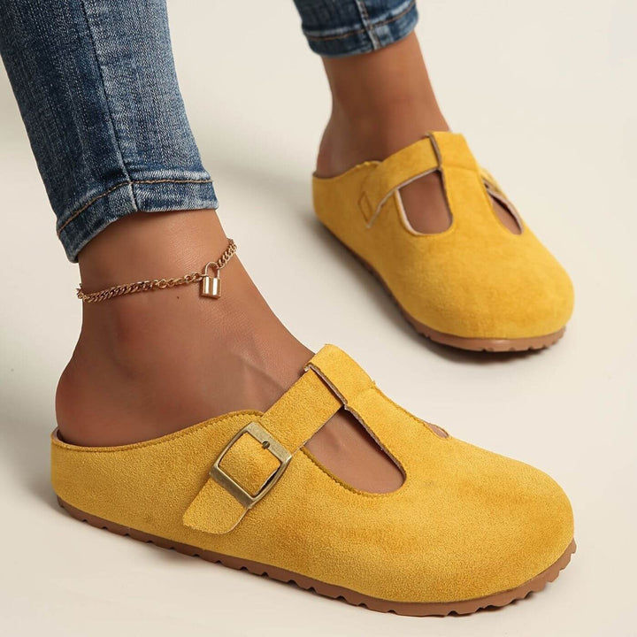 Yellow suede T-strap clogs with gold buckle worn on model's feet