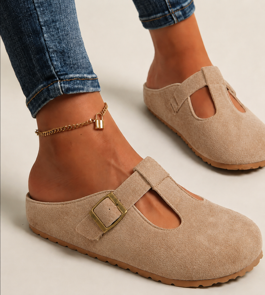 Beige suede T-strap clogs with gold buckle detail on model's foot