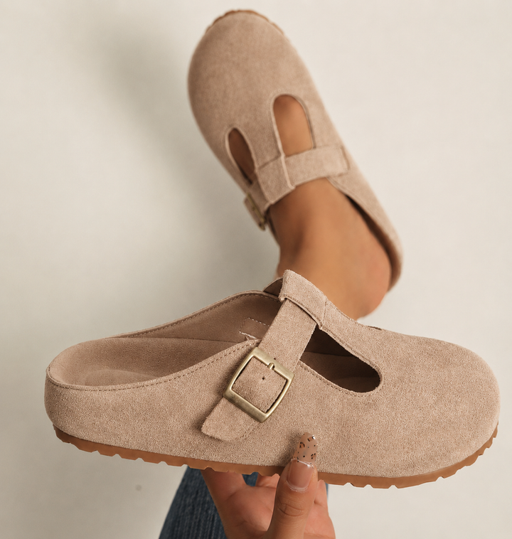 Beige suede clogs held up showing footbed, buckle, and rubber sole
