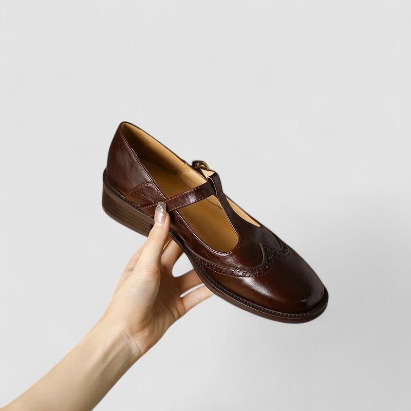 Brown leather T-strap Mary Jane shoe held up showing buckle and sole