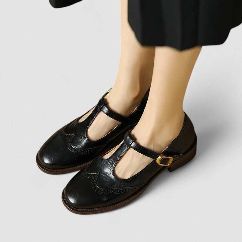 Black leather T-strap Mary Janes featuring perforated wingtip toe design