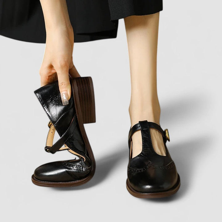 Black leather T-strap Mary Jane shoes held by hand showing heel detail