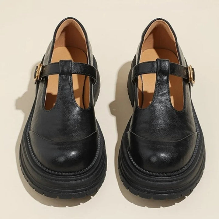 Top-down view of black T-bar Mary Jane shoes with gold buckle detail
