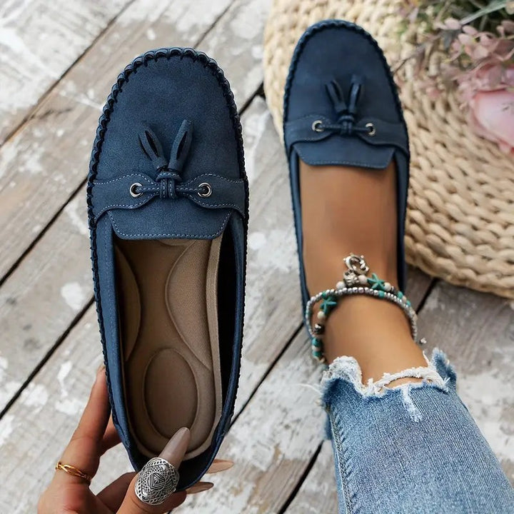 Navy suede tassel loafers displayed pair-wise on rustic wooden floor