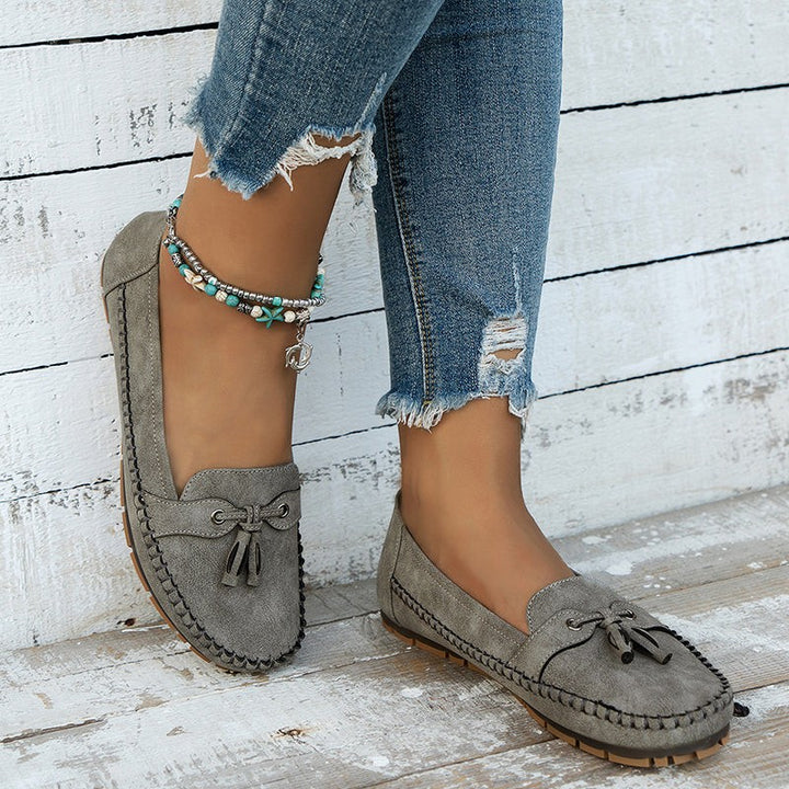 Gray suede tassel loafers worn with cuffed jeans on weathered wood