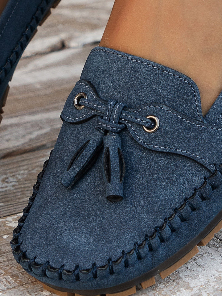 Navy suede loafer close-up showing tassel bow and whipstitch trim