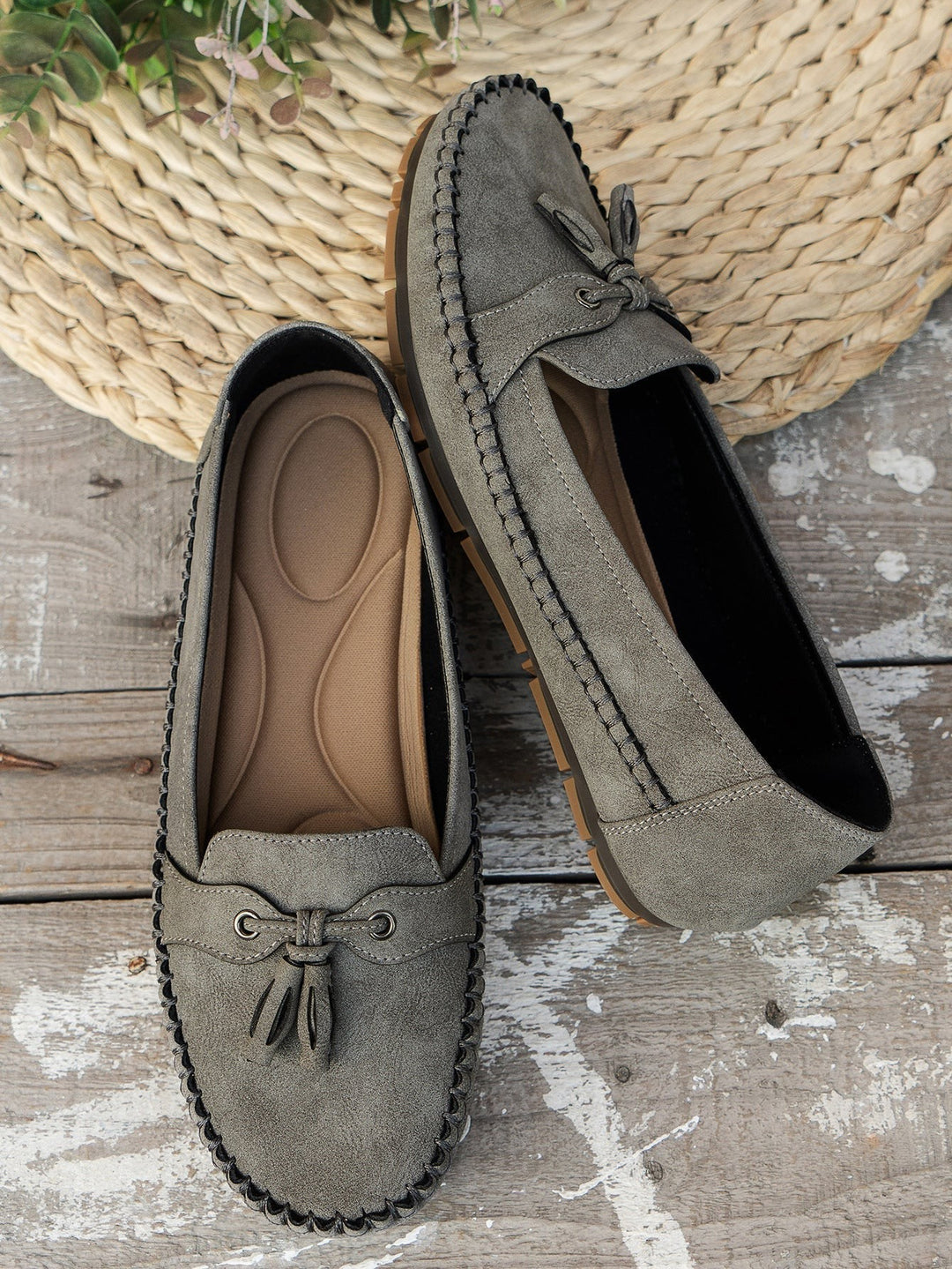 Olive gray suede tassel loafers displayed crossed showing sole tread