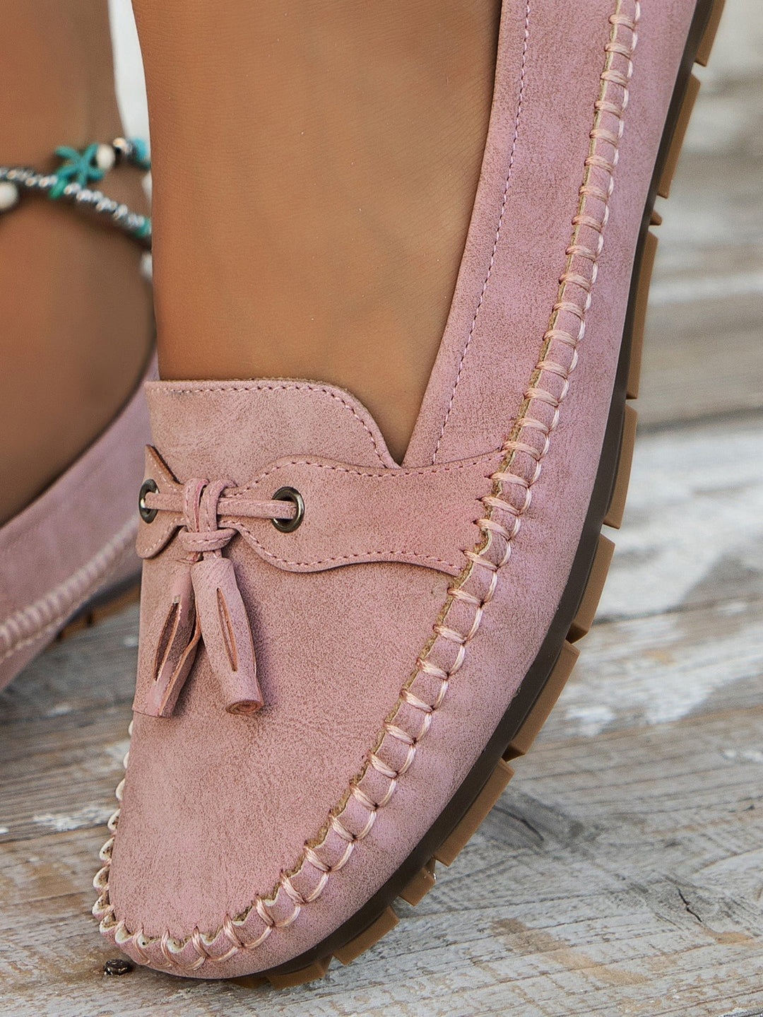 Blush pink suede loafer close-up highlighting tassel and stitched edge