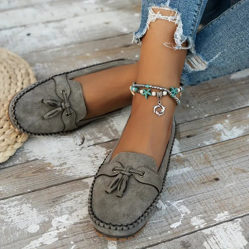 Gray suede tassel loafers styled with ripped jeans and beaded anklet