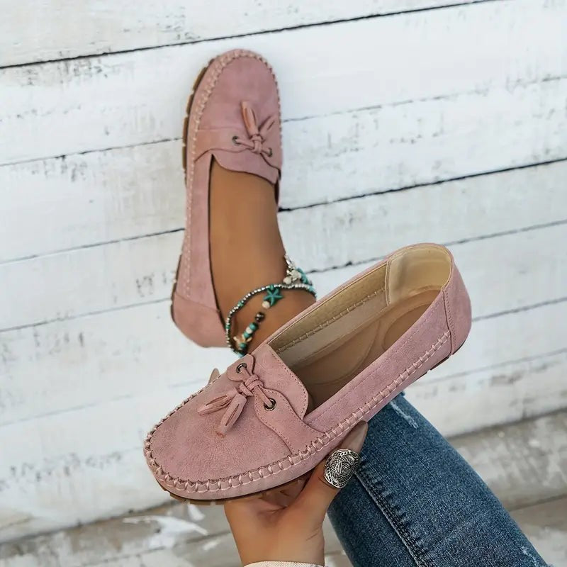 Pink suede moccasin loafers held by hand showing stitched sole detail