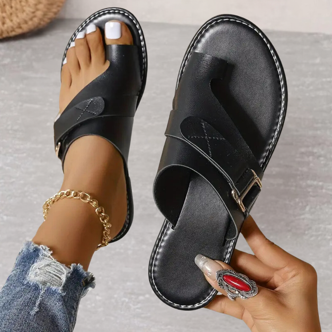 Black leather flat sandals with toe loop, buckle strap, and stitched trim