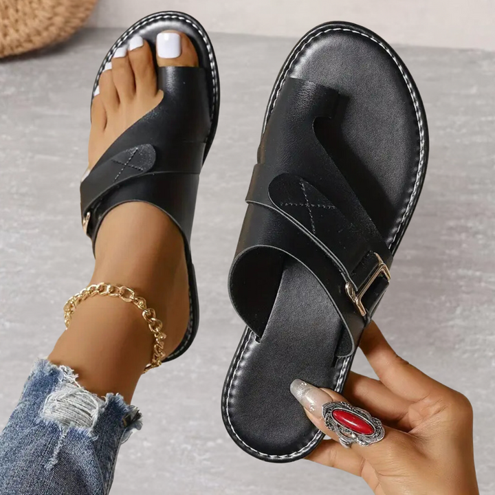 Black leather flat sandals with toe loop, buckle strap, and stitched trim