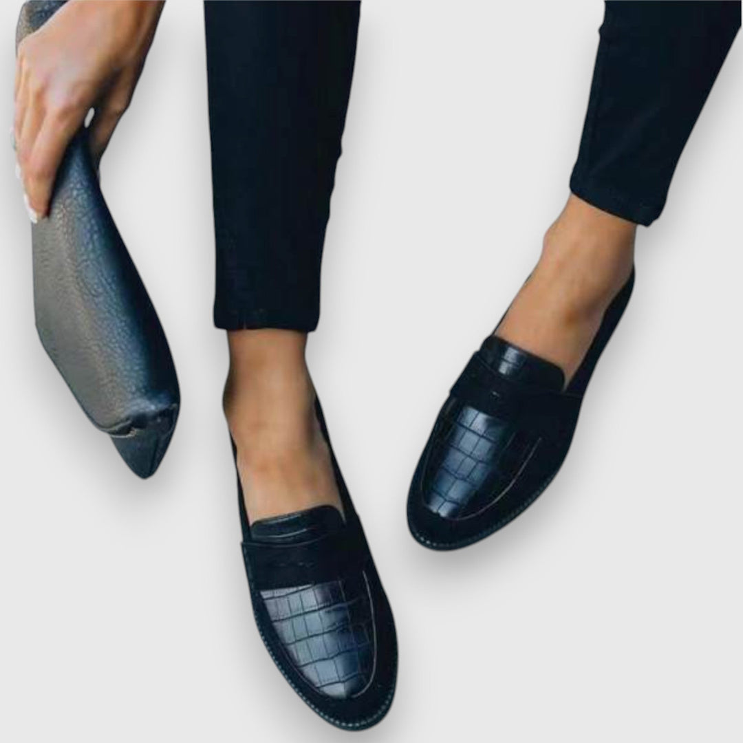 Model holding matching black clutch beside croc-print suede penny loafers