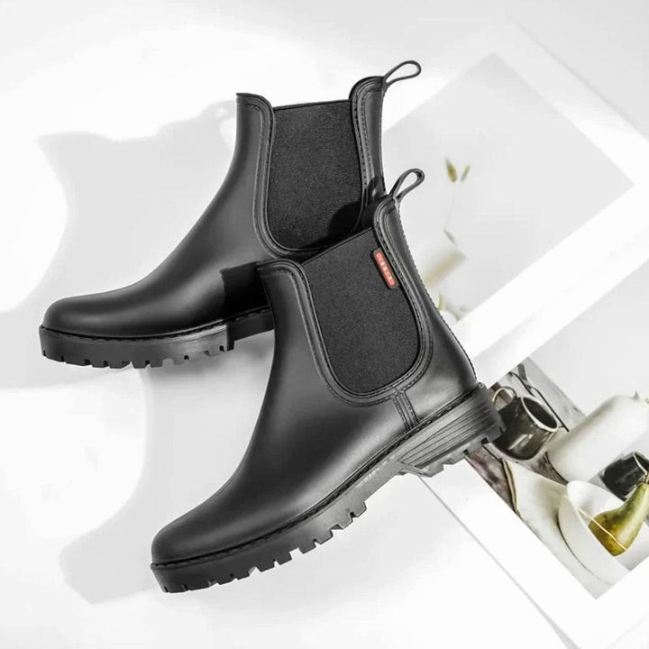 Black Chelsea boots arranged beside magazine props on marble-effect surface