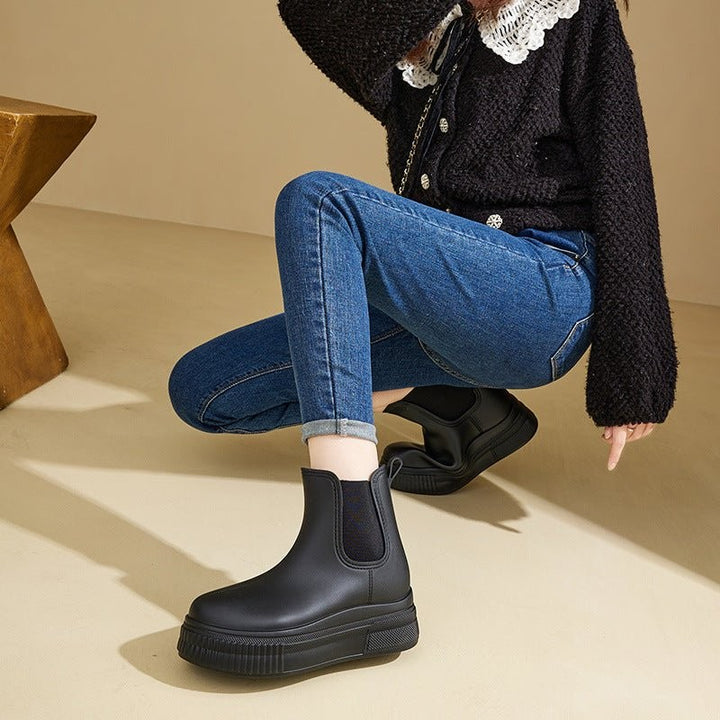 Model crouching in black Chelsea platform rain boots with denim jeans