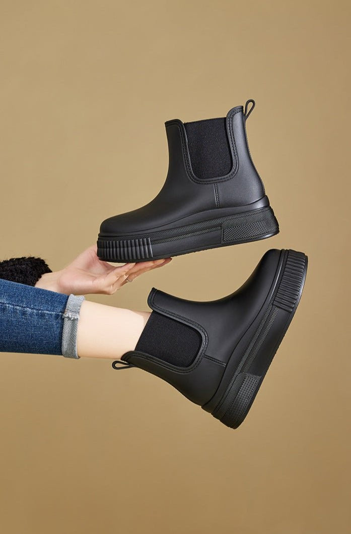 Black Chelsea rain boots held in hand showing platform sole and elastic panel