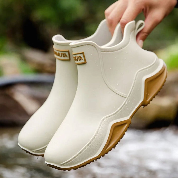 Cream Chelsea rain boots with tan rubber sole, held up outdoors
