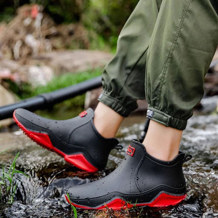 Black waterproof ankle boots with red sole, worn beside a stream