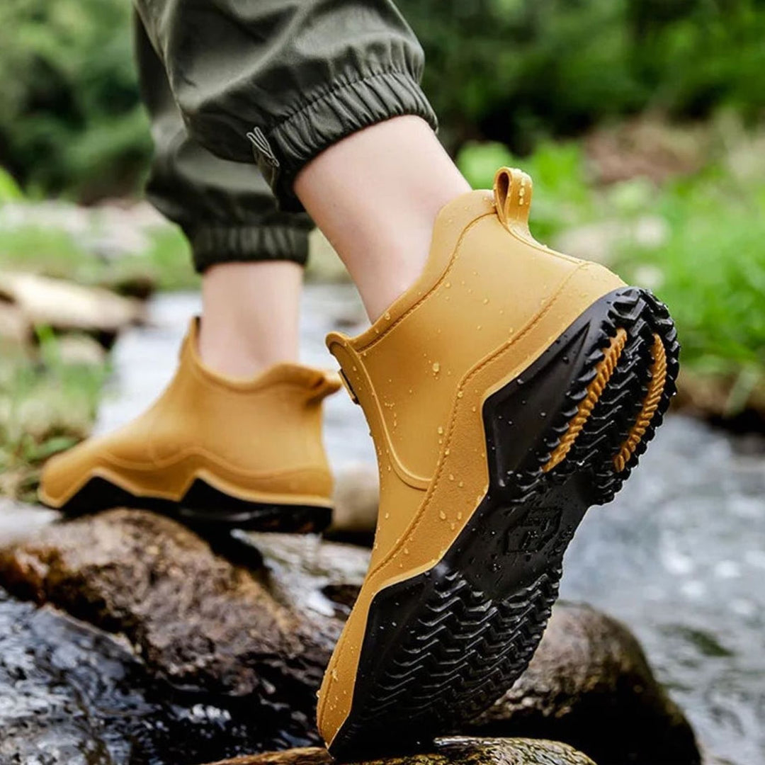 Mustard yellow Chelsea rain boots with black tread, worn crossing rocks
