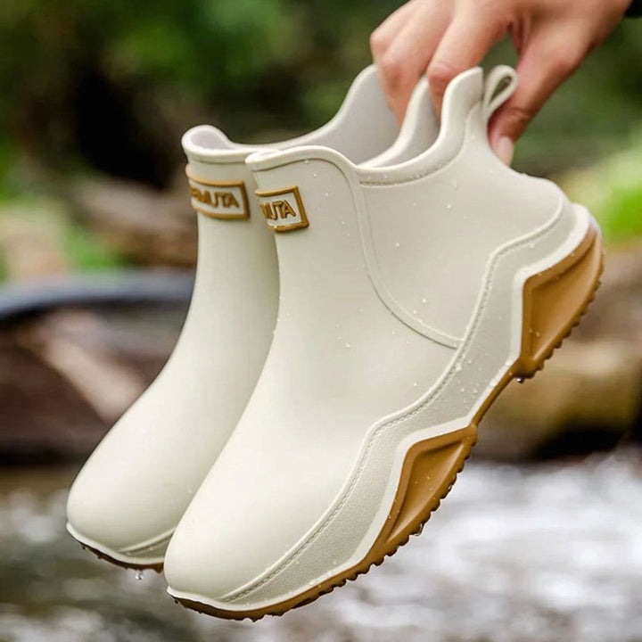 Cream waterproof Chelsea boots with tan sole, held above flowing water