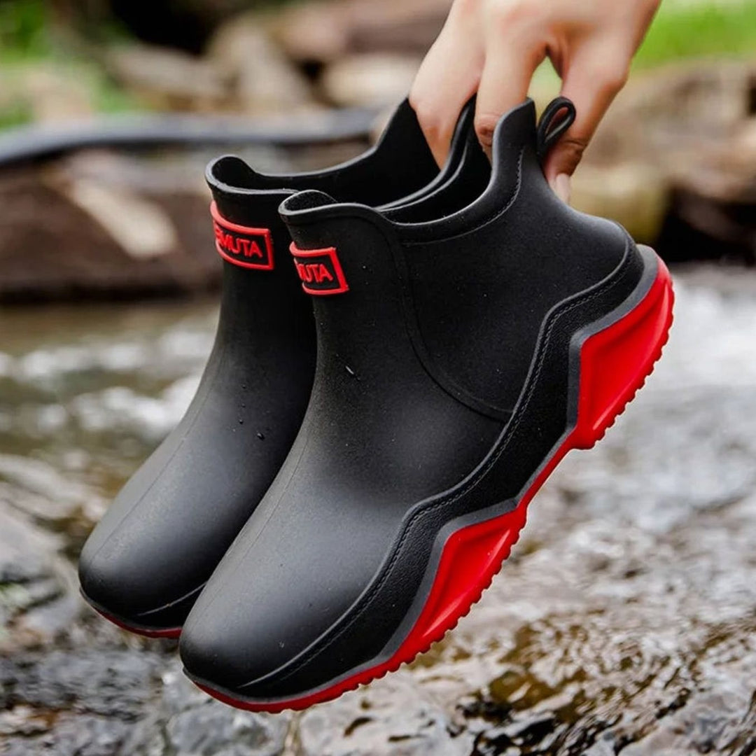 Black Chelsea rain boots with red sole trim, held up outdoors