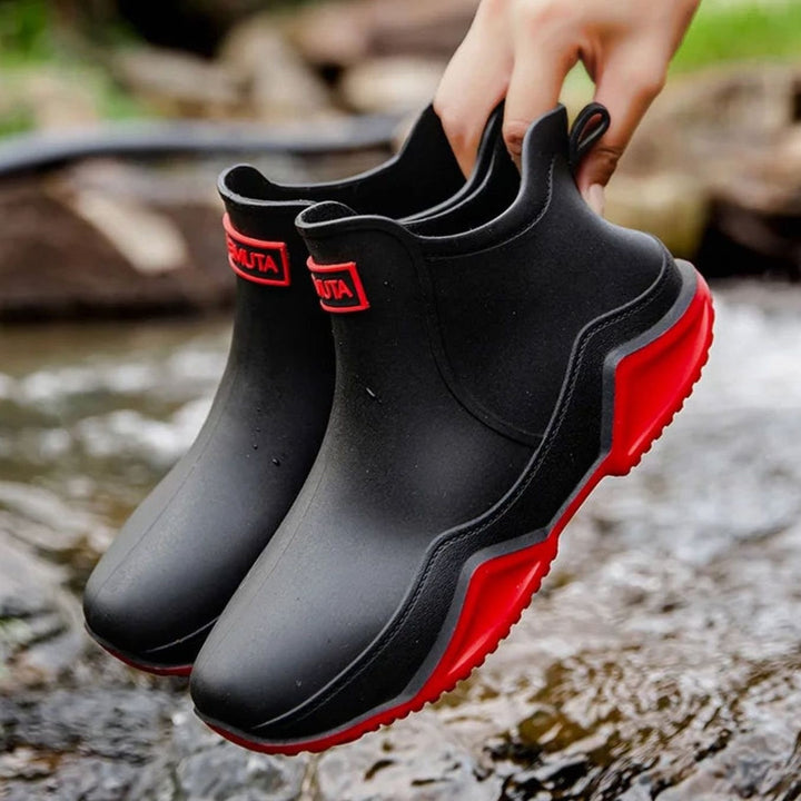 Black Chelsea rain boots with red sole trim, held up outdoors