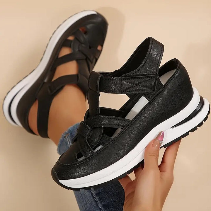 black closed-toe wedge sandals with woven strap detail, shown in hand