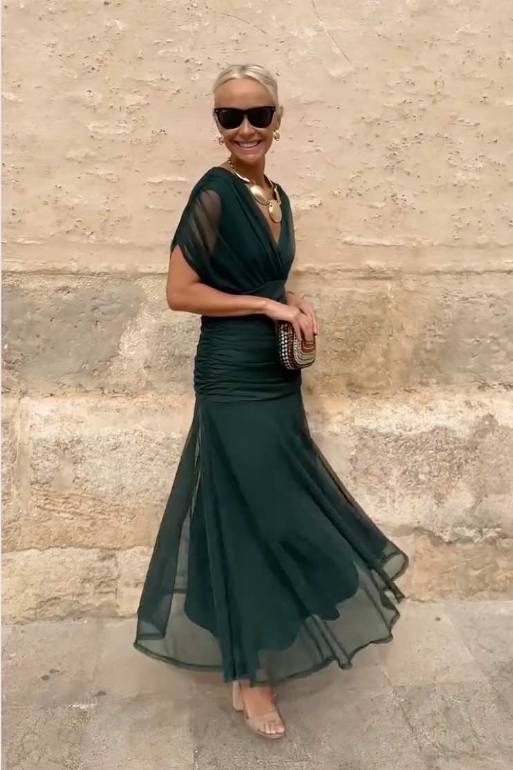 Side view of emerald green maxi dress with sheer sleeves and flared hemline